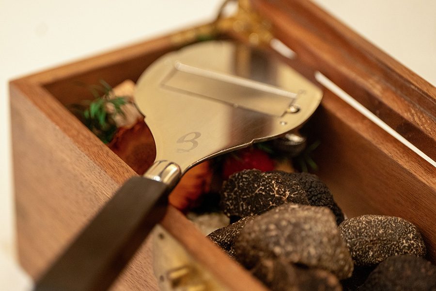  A wooden box containing black truffle with a steel truffle shaver. 