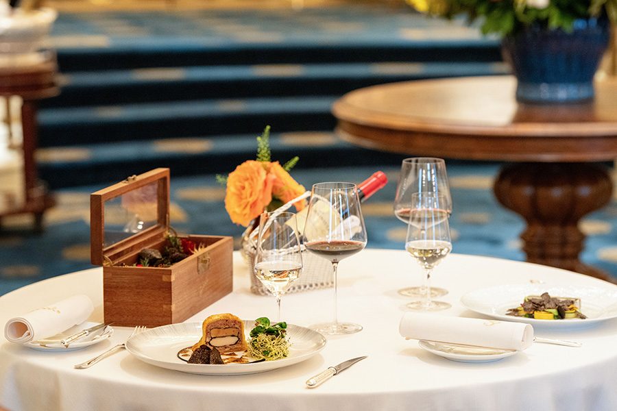 Plates with dishes from Gaddi’s Australian truffle menu on a table paired with glasses of red and white wine at Gaddi’s, The Peninsula Hong Kong. 