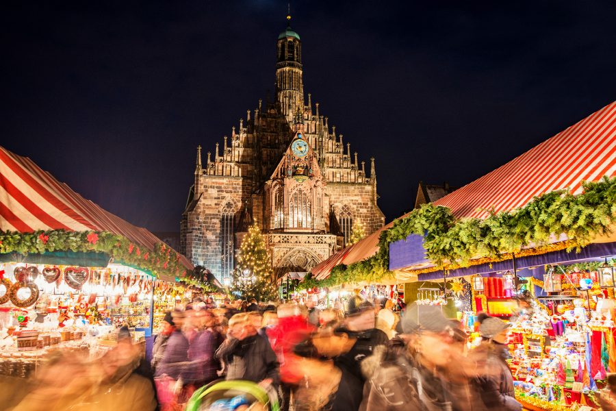 The crowded Nuremberg Christkindlesmarkt at night with the Frauenkirche in the background.