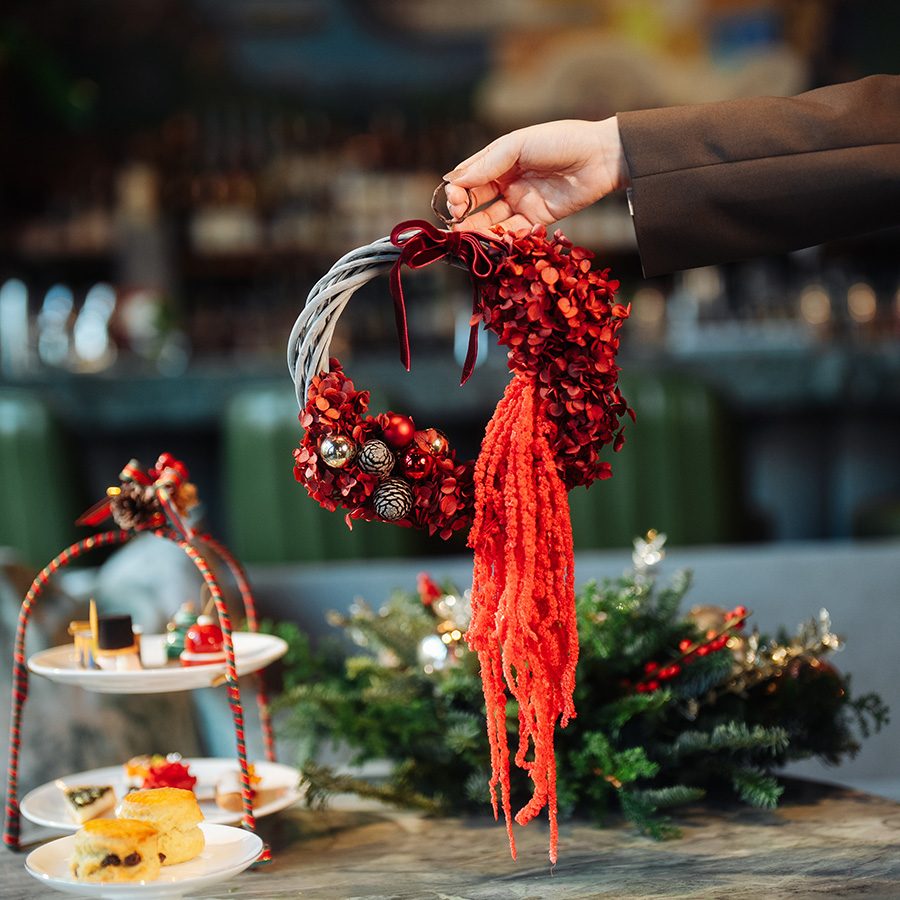 A person holding up a Christmas wreath next to a high tea set from Blooms & Blossoms.
