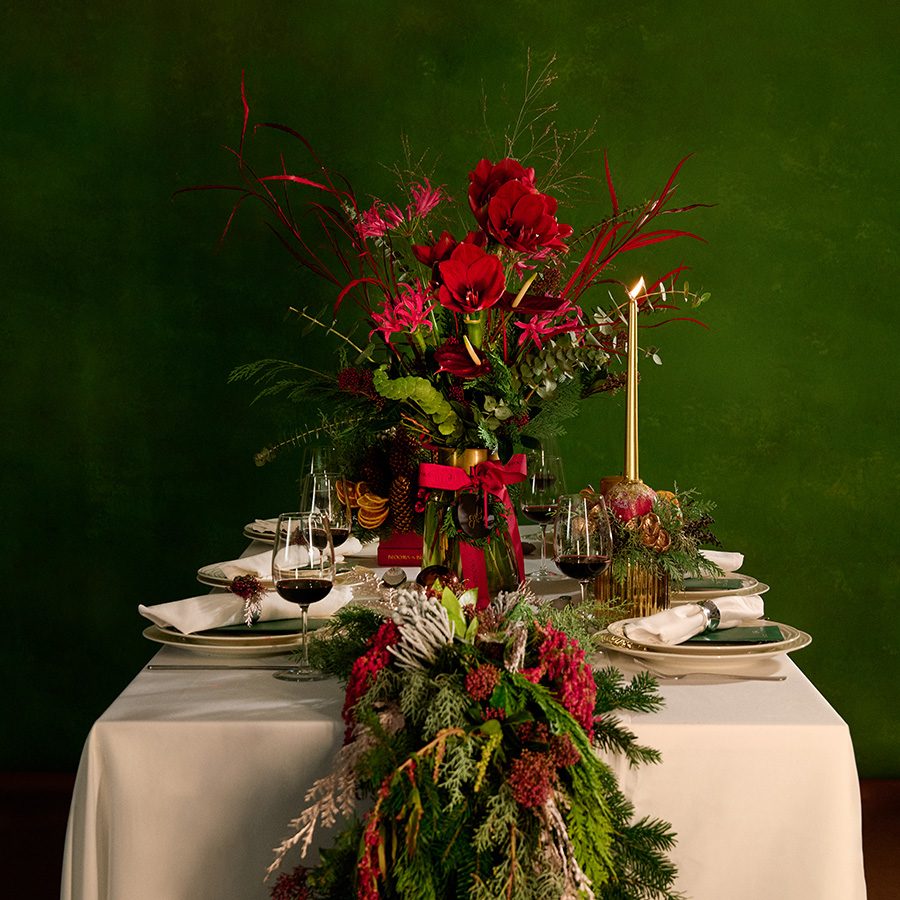 A table set up for a Christmas dinner, decorated with pine tree floral arrangements and candles from Blooms & Blossoms in Hong Kong. 