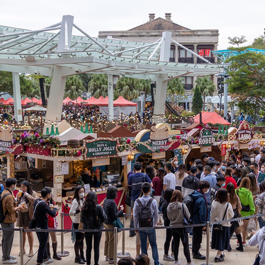 An overview of the Stanley Plaza Christmas Market. Crowds of people are lining up for booths sporting lights and Christmas décor, selling food and gifts. 