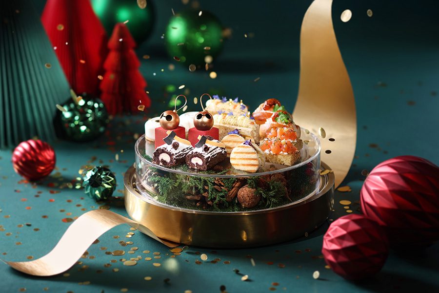 A  glass dish filled with Shangri-La Boutique’s Christmas-themed bite-sized cakes and sweets next to baubles and tree-shaped decorations, serenaded by a sprinkling of gold confetti. /