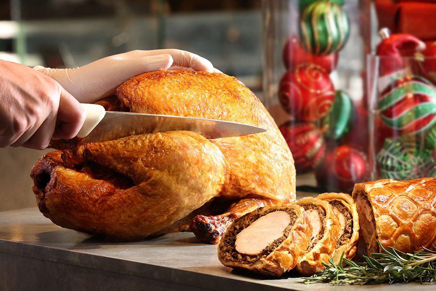 A person holding a knife carving into a Christmas roast turkey next to slices of beef wellington.