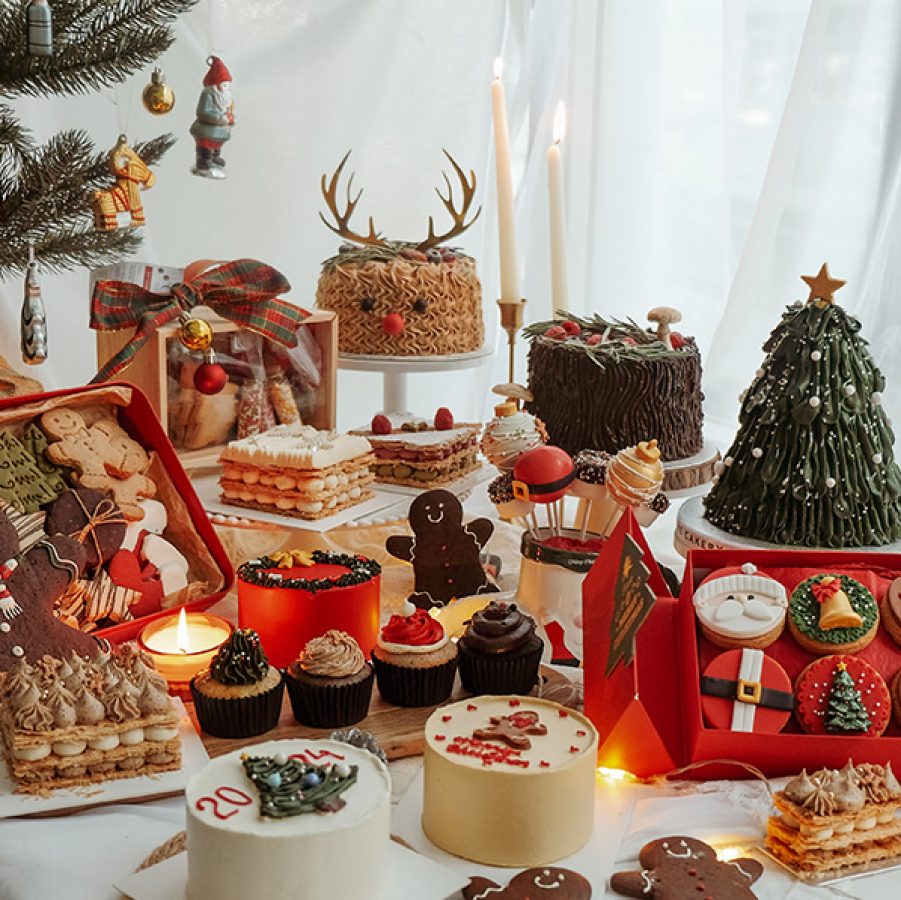 A spread of Christmas-themed pastries, cakes and gingerbread cookies on a white table, made by The Cakery in Hong Kong. 