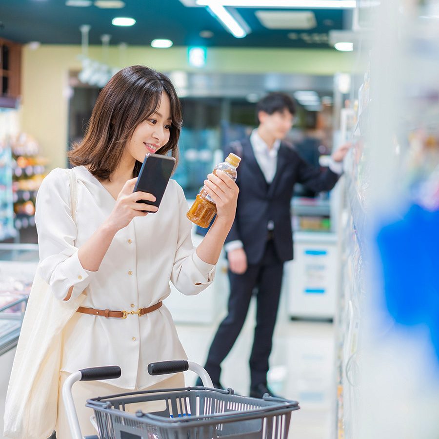A woman comparing a bottle of dressing to her phone screen while at the supermarket shopping.