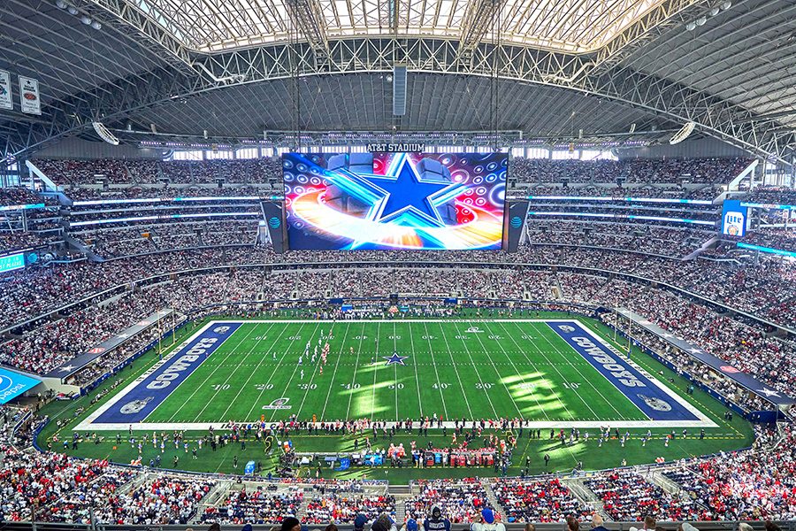 A wide view of the inside of the AT&T Stadium during a sports event, featuring a green pitch and stands filled with spectators.  