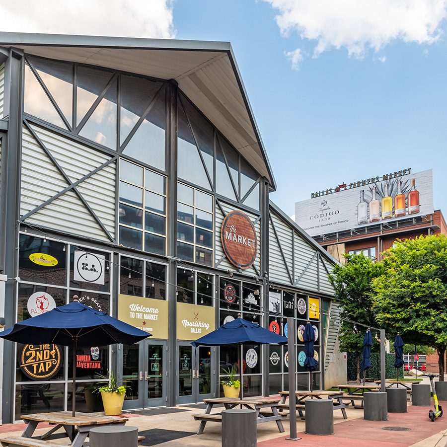 The entrance of the Dallas Farmers Market, a steel warehouse-style building, against a blue sky