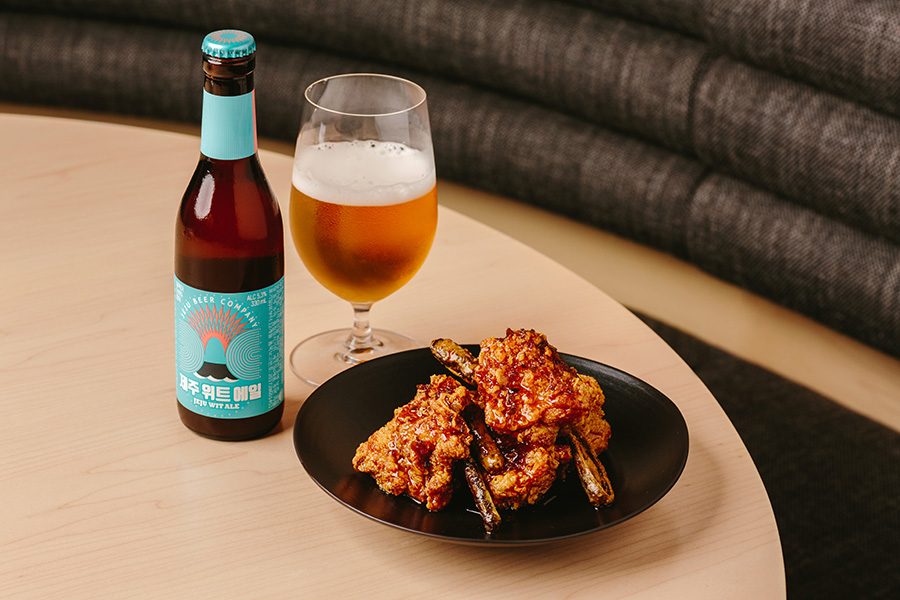 A plate of Korean fried chicken on the bone with Yuza Jang sauce with a bottle of craft beer poured into a glass on a dining table at Michelin star restaurant Hansik Goo in Hong Kong.