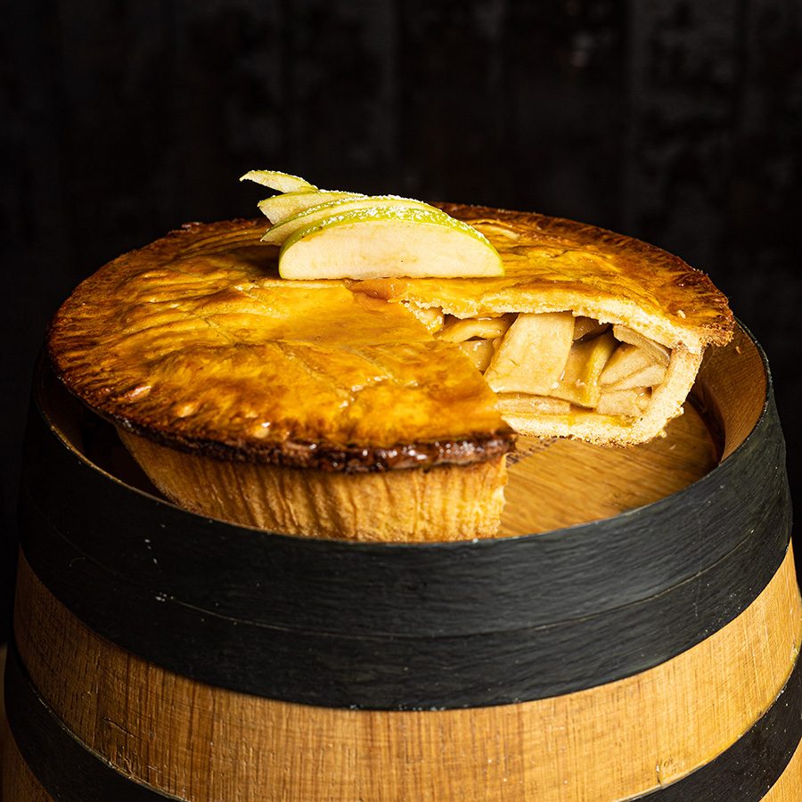 A whole apple pie filled with apples on a top of a wooden barrel.