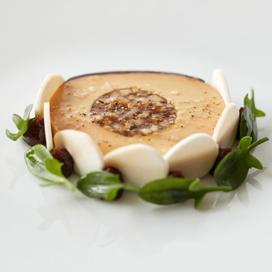 A dish at Sézanne, Tokyo, featuring small white discs and leaves circling a brown mousse. 
