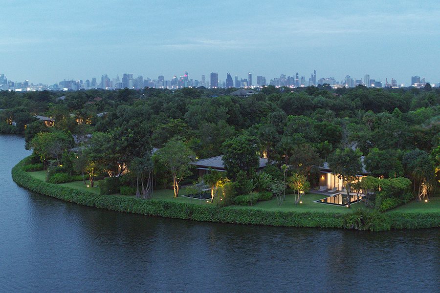 A bird’s eye view of RAKxa Intergrative Wellness hotel and resort surrounded by lush greenery by the sea in the evening.