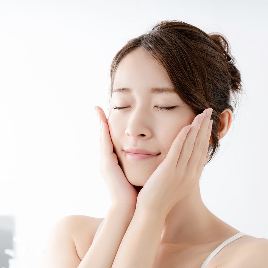 Happy Asian woman placing her hands on her face after skincare routine 