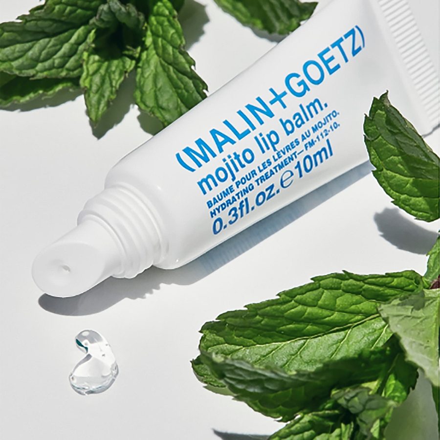 A white tube of Malin+Goetz mojito lip balm with mojito leaves in the background 