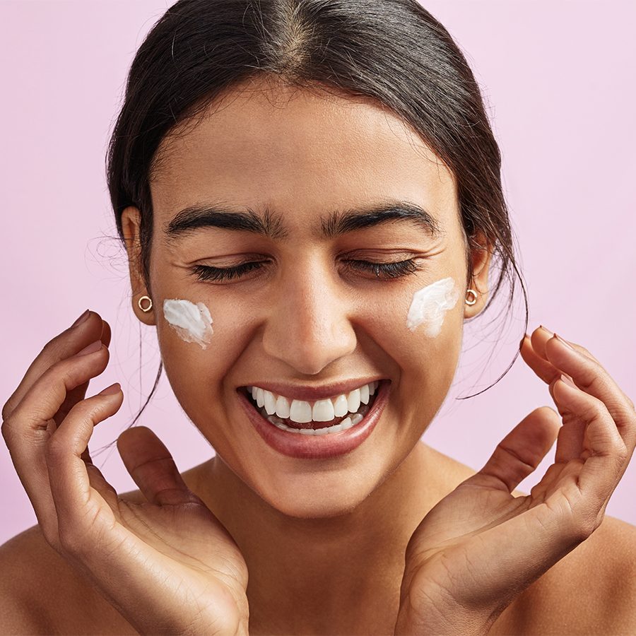 Asian woman laughing while applying moisturizing cream on her face 