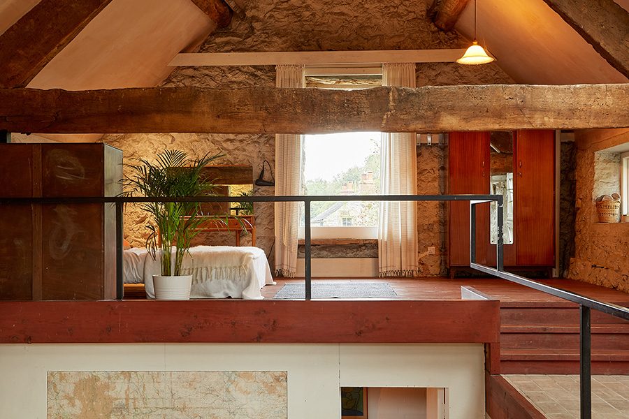 A mezzanine bedroom with wooden beams and stone walls in Rewilded Retreats, Derbyshire. 