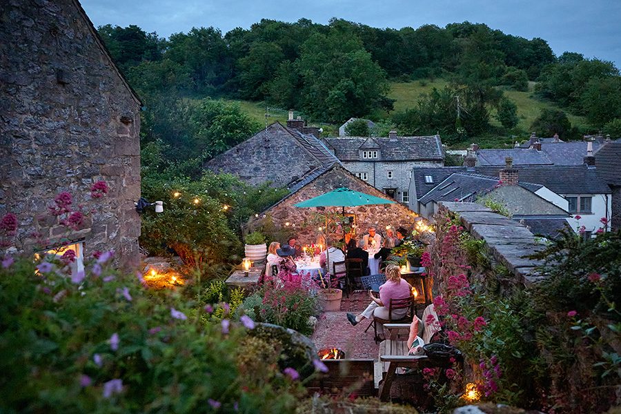 People sitting at tables on a terrace at dusk at Rewilded Retreats, Derbyshire.