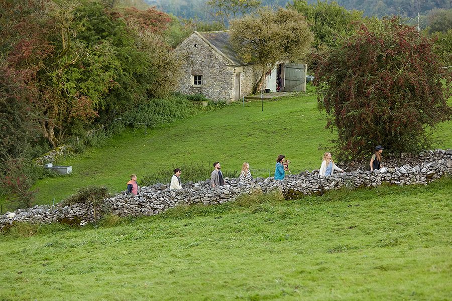 People walking along a country road past a stone cottage at Rewilded Retreats, Derbyshire. 