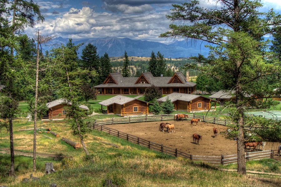 Exterior of the Three Bars Guest Ranch with log cabins, horses and trees. 