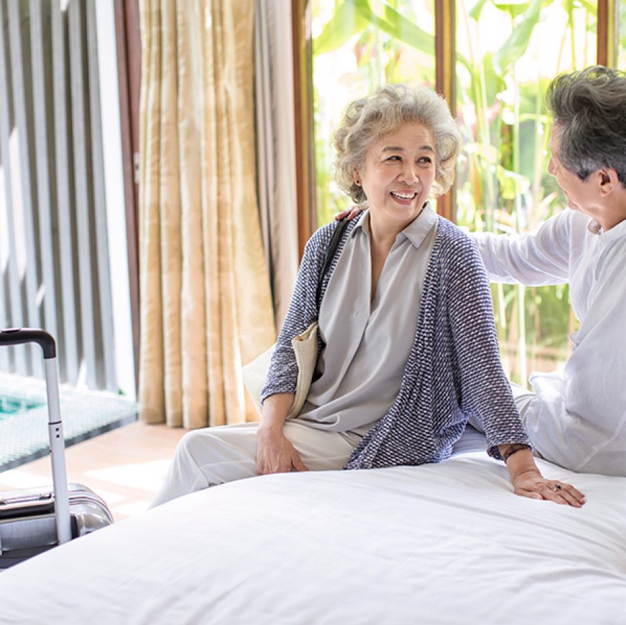 An older couple on holiday smiling in a hotel room with luggage
