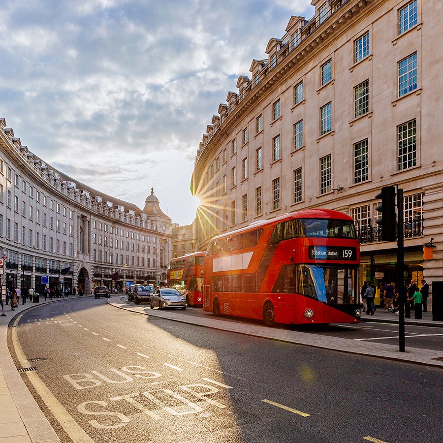 A street view of London featuring a double decker bus picking up passengers on a sunny day