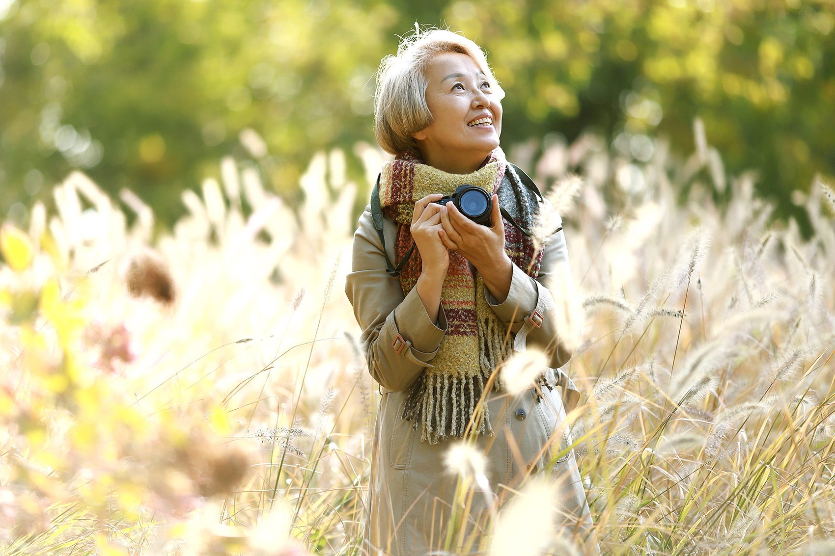 Older adult wearing a coat and scarf, smiling in an open field on a sunny day 