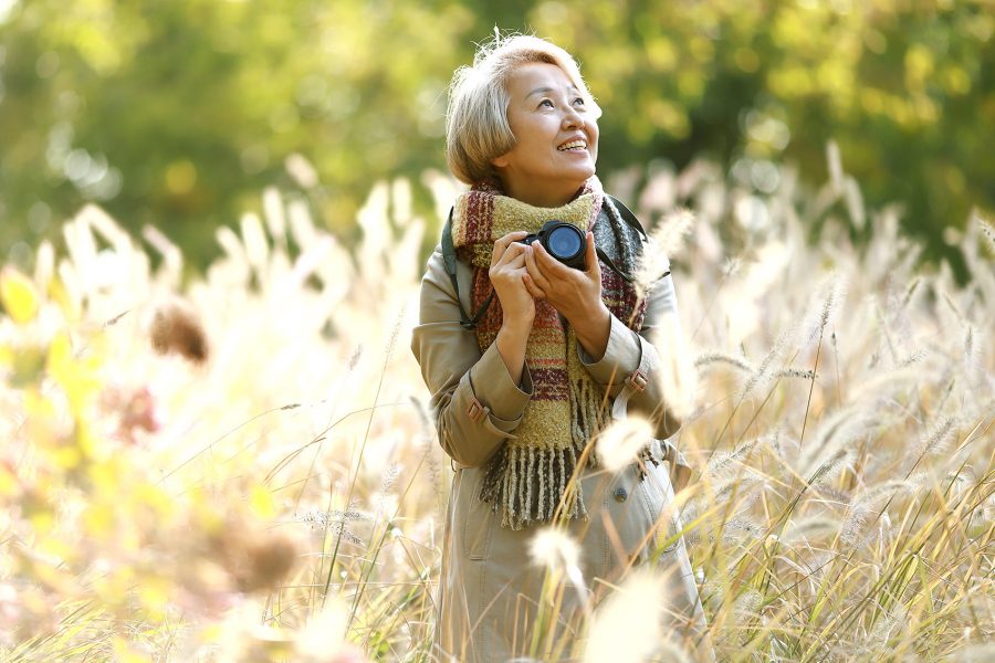 Older adult wearing a coat and scarf, smiling in an open field on a sunny day 