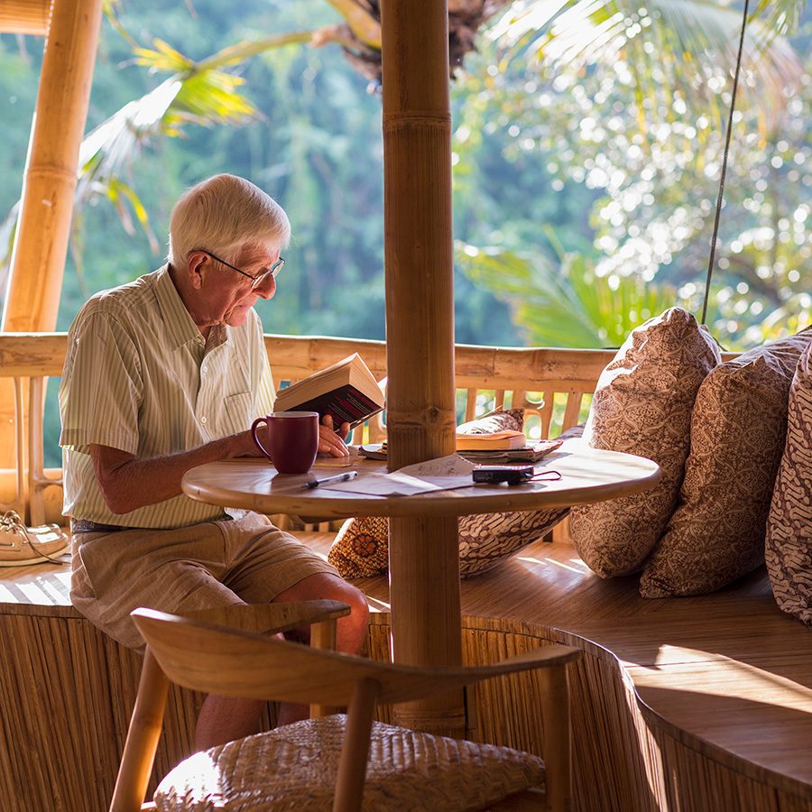 An older man reading a book and drinking coffee in an open air cabana cafe 
