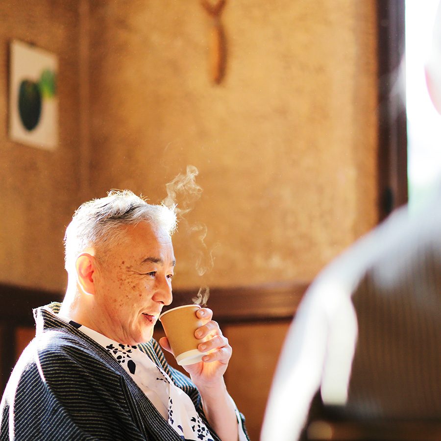 An older man smiling and drinking hot tea in a cafe at daytime