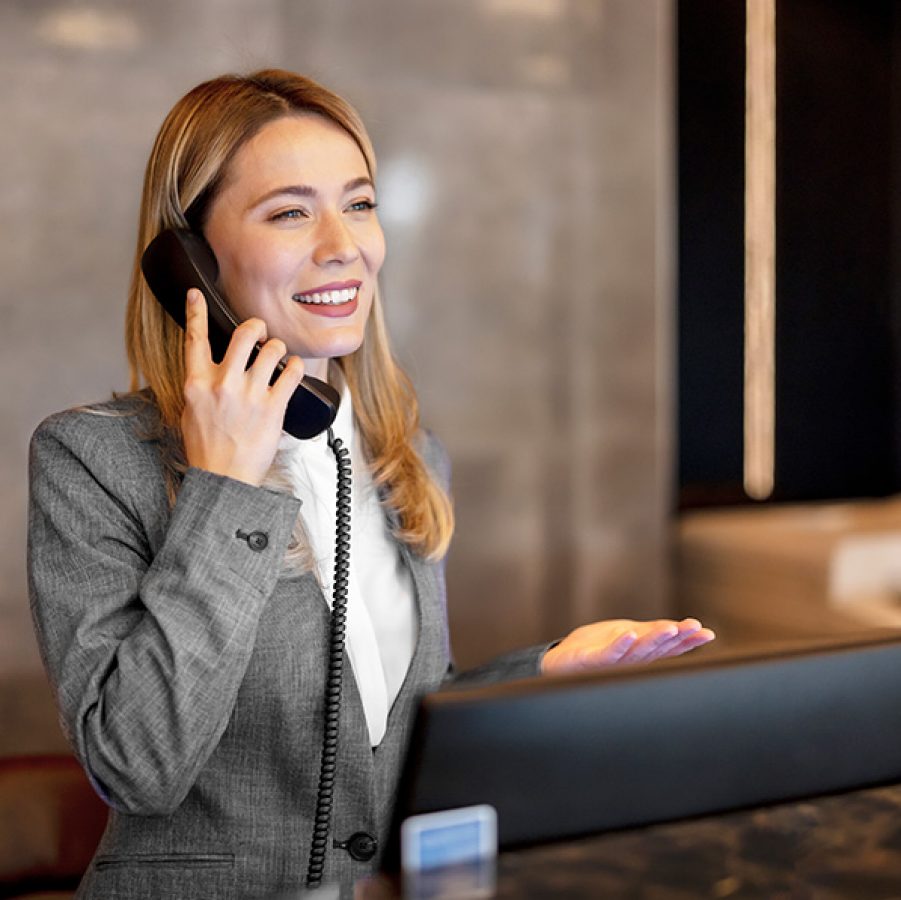 A woman working at the receptionist smiling and answering a call 