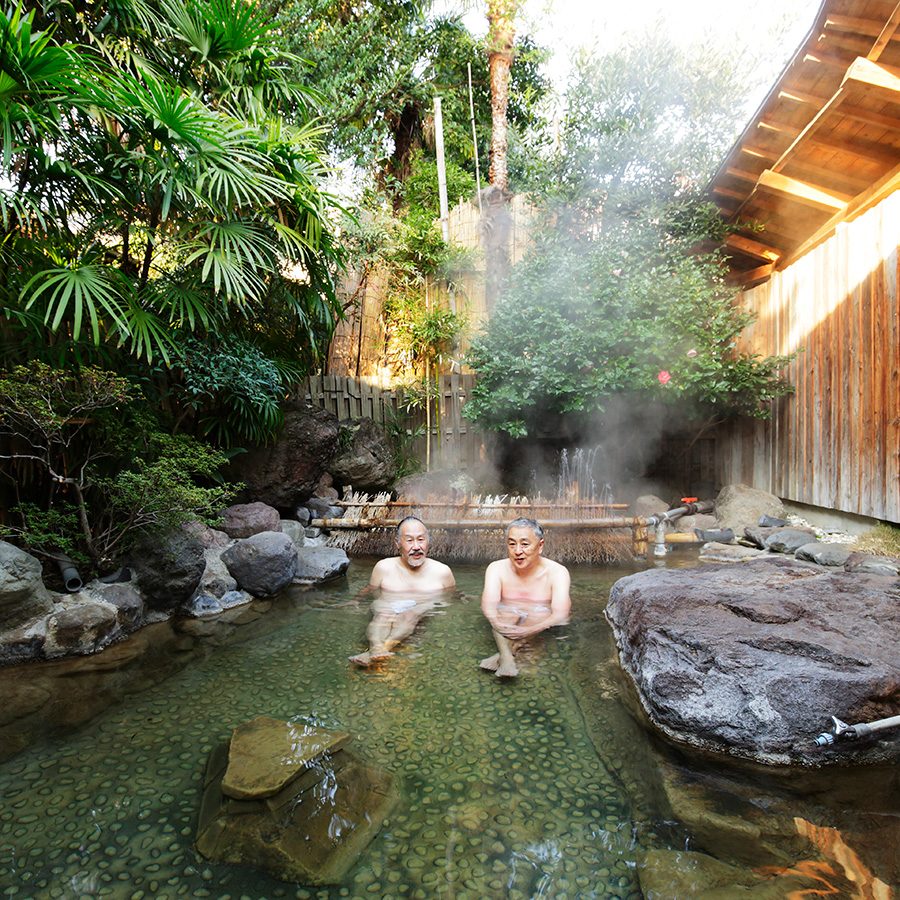 An older couple relaxing in a Japanese outdoor hot spring during daytime 