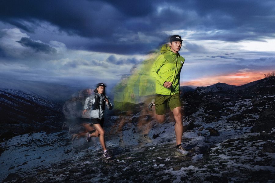 A man and a woman jogging across a mountainous landscape, wearing The North Face clothing.