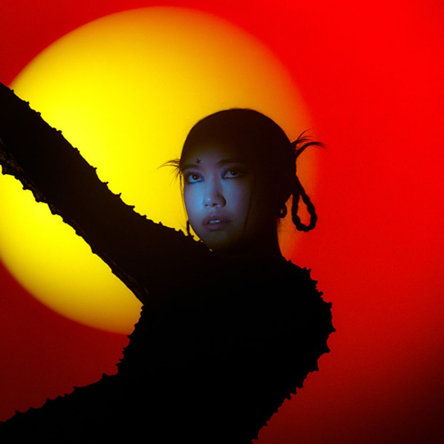 Hong Kong British singer Mui Zyu is pictured silhouetted with only a small part of her face show against a yellow and red background.