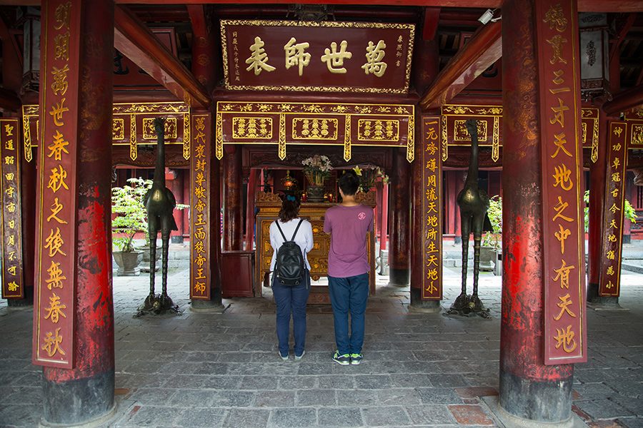 A man and a woman stand in front of the shrine at Hanoi’s Temple of Literature in the daytime.