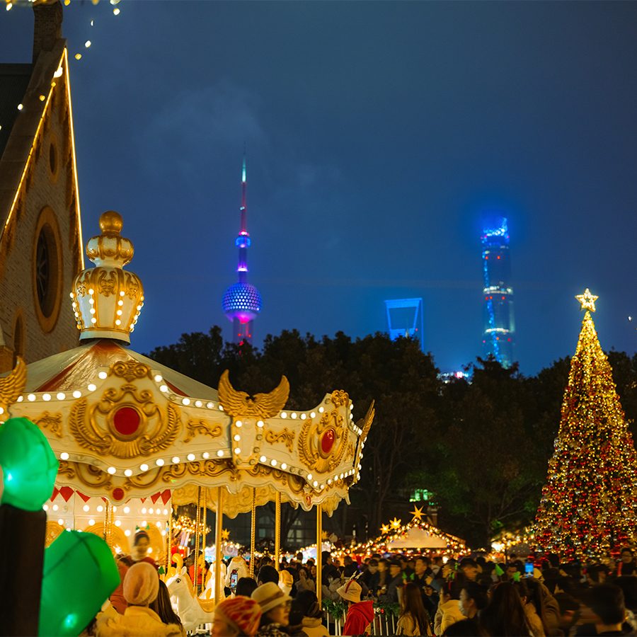 A nighttime Christmas display featuring a carousel and a big Christmas tree with the skyline of Shanghai, China in the background. 