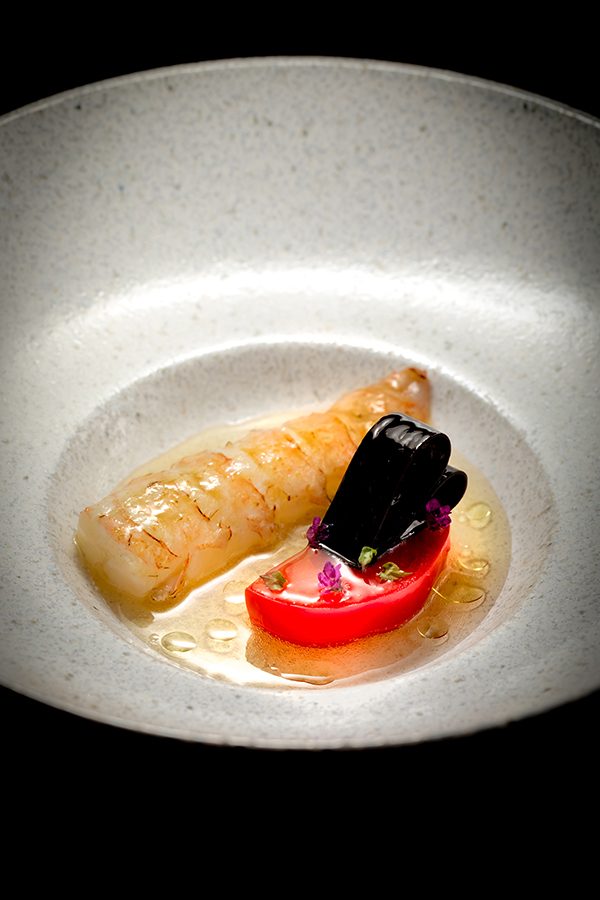A close-up of a slice of langoustine on a white dish. 