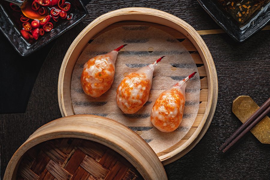 Three prawn dumplings are displayed in a bamboo steam basket .