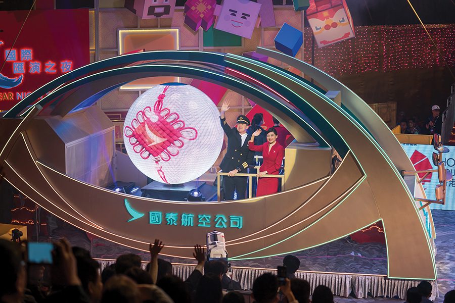 A Cathay Pacific flight attendant and pilot dressed in uniform standing on stage with Chinese New Year decorations. 