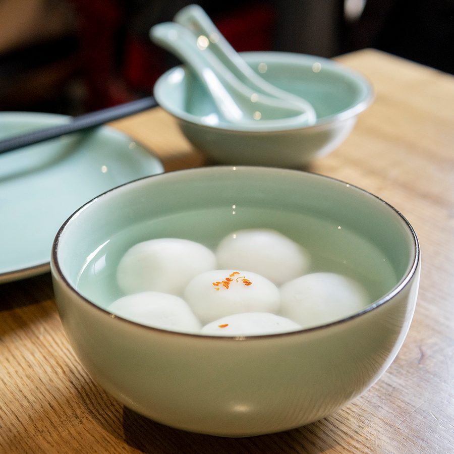 Glutinous rice balls in a celadon bowl, with another bowl, spoon, chopsticks, and plate behind it.