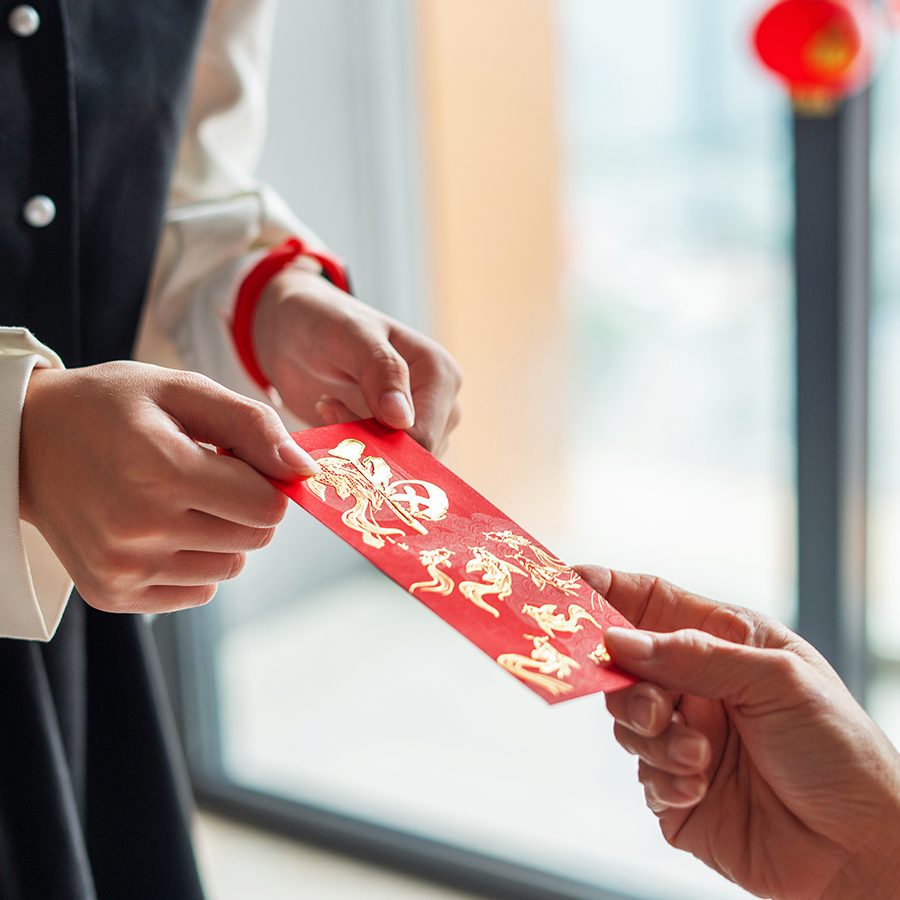 Close-up of a person handing a red envelope to another person. 
