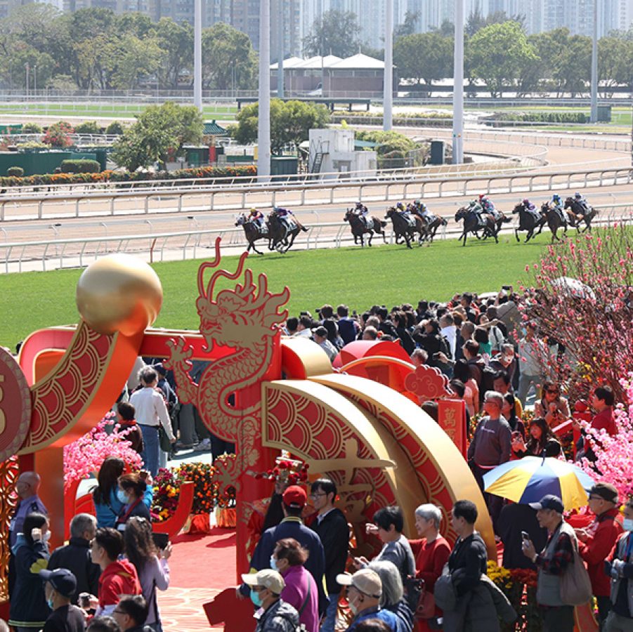 Visitors and jockeys at Chinese New Year Race Day. The venue is decorated with pink flowers and a large, red-and-gold dragon arch. 