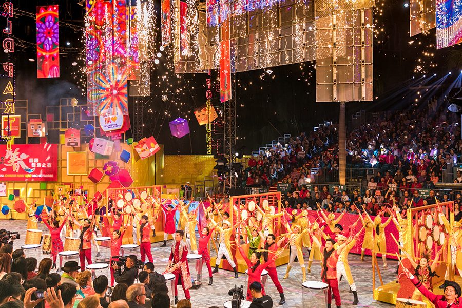 People dressed in red and gold performing on stage, with Chinese New Year decorations hanging above them. 