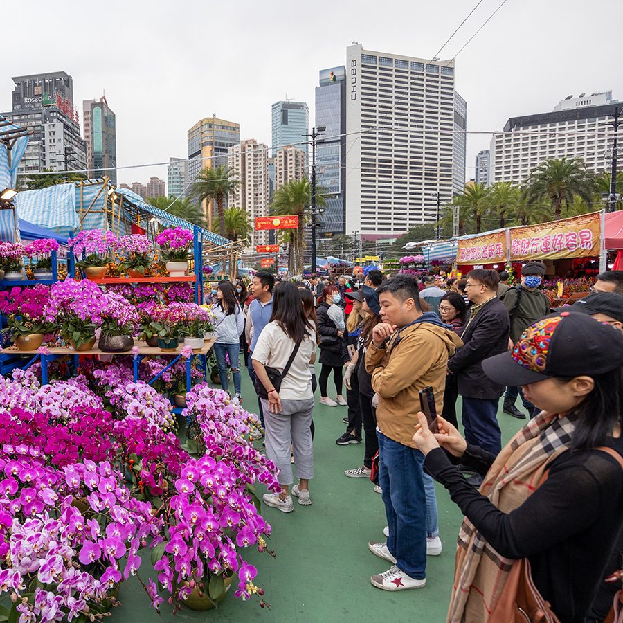 People standing in front of a booth with lots of pink flowers at a flower market. 