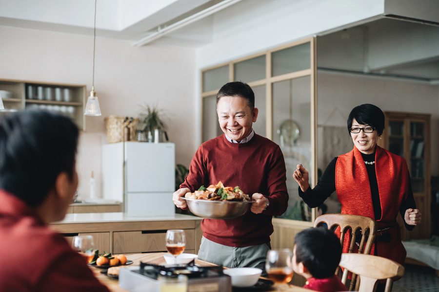 Man carrying over a bowl of food to family gathered around the dining table all dressed in red clothing.