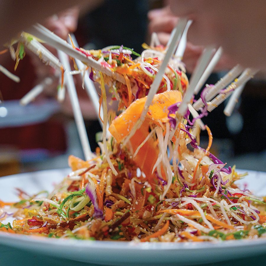 People using chopsticks collectively toss a lo hei salad.