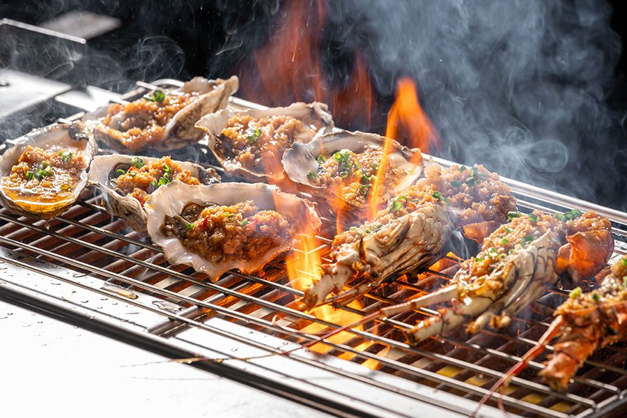 A closeup of shellfish and seafood being grilled over charcoal fire, served at Angsana Zhuhai Phoenix Bay resort hotel. 