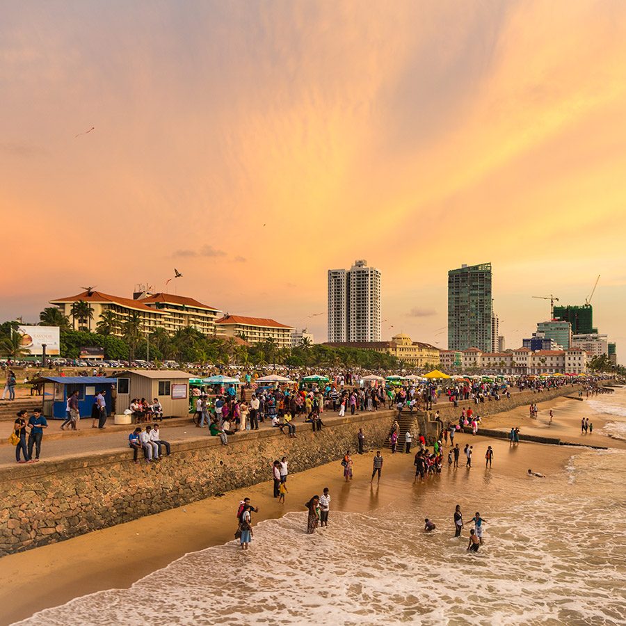 People on the beach at Galle Face Green, with buildings in the distance.