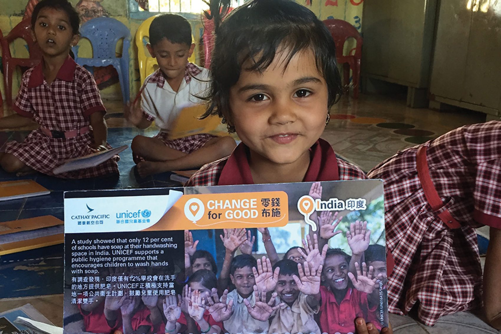 A young Indian child smiling and holding a Cathay Pacific and Unicef Hong Kong Change for Good leaflet.