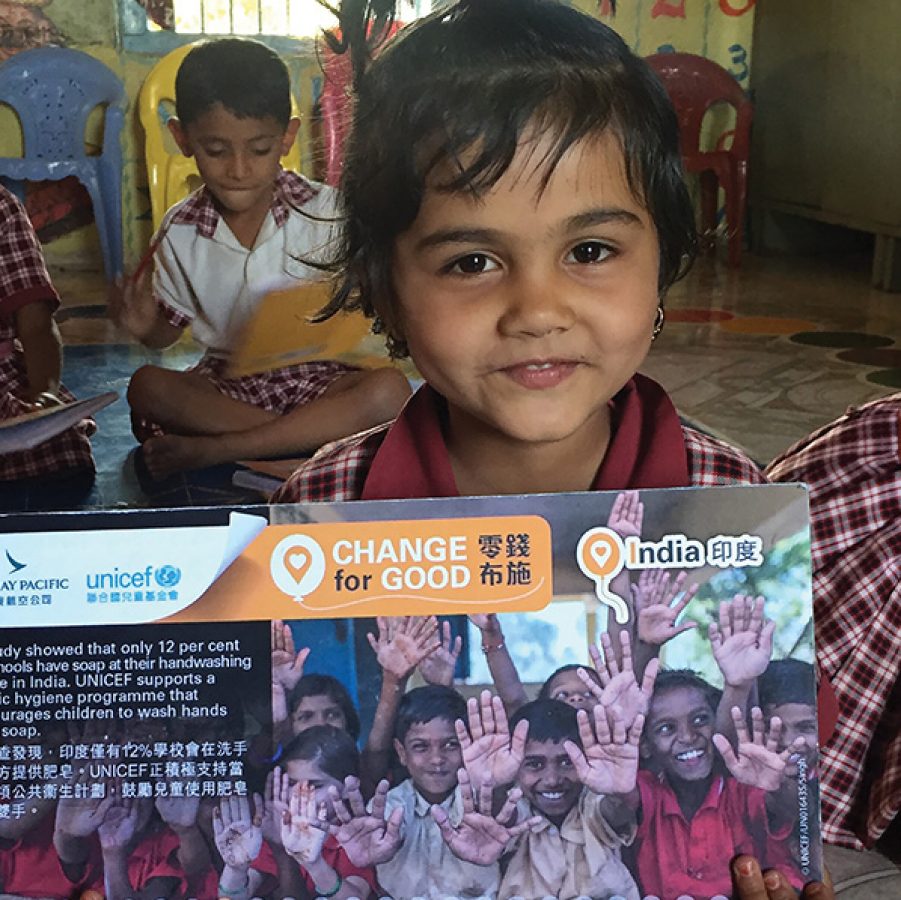 A young Indian child smiling and holding a Cathay Pacific and Unicef Hong Kong Change for Good leaflet.