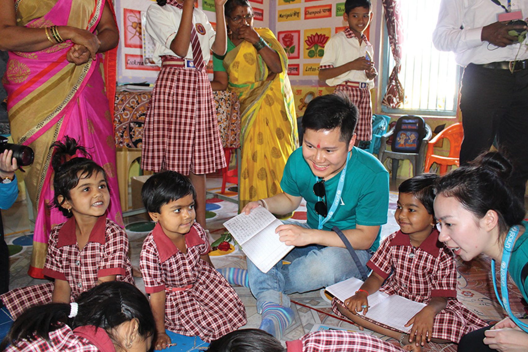 A man in green from Unicef Hong Kong smiling teaching a group of children in a classroom.